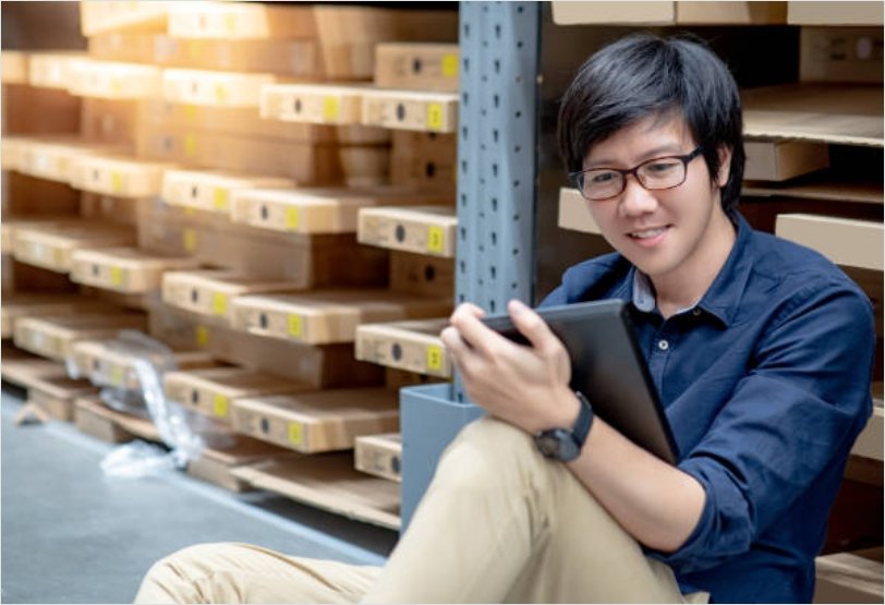 a young colleague is doing stocktaking of product in cardboard box on shelves in warehouse